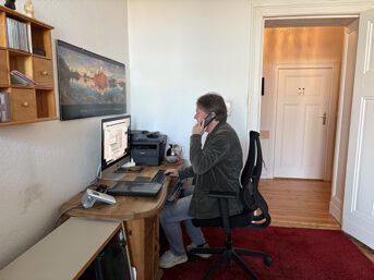 Picture: Thomas Abel at his desk in front of the computer with a phone in his hand